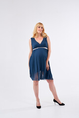 A pregnant woman is wearing a blue dress and standing in front of a white background. She is wearing black heels and has blonde hair