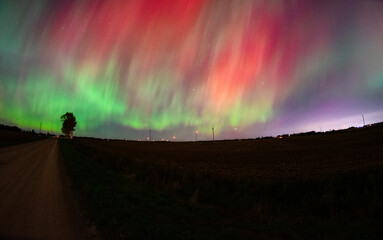 Green, yellow, and red aurora over a rural country road with a city in the distance