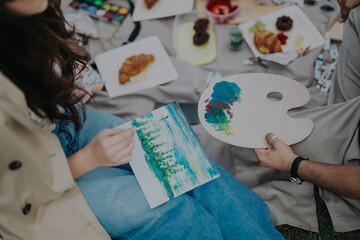 Two people engaging in painting and enjoying food during an outdoor picnic. Artistic creativity and...