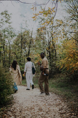 A group of friends enjoys a leisurely walk through a forest path, surrounded by lush greenery and autumn leaves. They embrace nature and companionship on a relaxing day off.