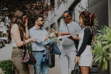 Diverse group of young business people engaged in a discussion outside, sharing ideas and reviewing...