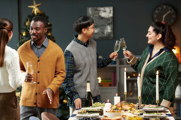Side view of cheerful man clinking glasses with female friend at dining table set with festive food, while chatting and celebrating Christmas together in living room