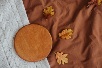 Autumn leaves scattered on a warm fabric with a wooden round platter in a cozy setting