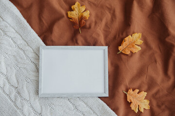 Cozy autumn setting with a blank frame and colorful leaves on textured fabric