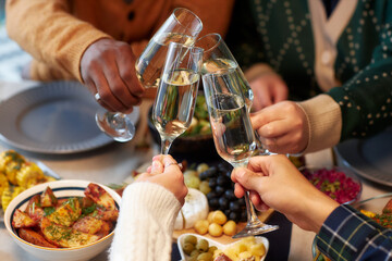 Cropped shot of people raising toast clinking glasses with champagne at friends gathering while...