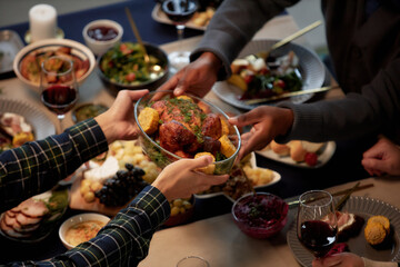 Cropped shot of man passing homemade roasted chicken to friend at dining table served with variety...