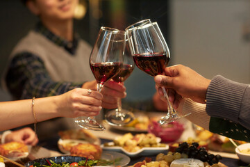Cropped shot of friends clinking wine glasses sitting at festive dining table at home dinner while celebrating Christmas, copy space