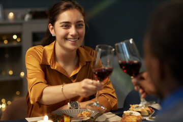 Medium shot of cheerful woman clinking wine glasses celebrating Christmas with friend sitting together at dining table in living room, copy space