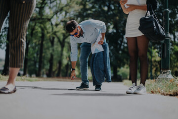 A group of business people casually interact in a park, with one person bending to pick something up. The scene conveys relaxation and teamwork in an outdoor environment.