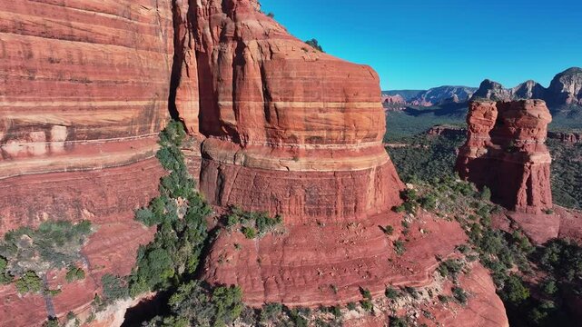 Aerial Sedona Arizona red mountain steep cliff slide 1. Red sandstone mountain formations. Glow in brilliant orange and red above pine forests. New Age industry Harmon Convergence or spiritual vortex.