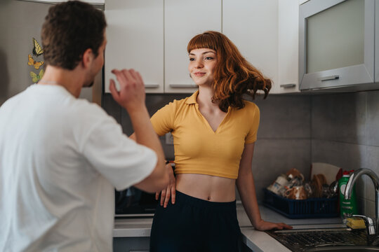 A young couple enjoying a lively conversation in their contemporary kitchen, creating a warm and friendly atmosphere. The space is filled with natural light and casual vibes.