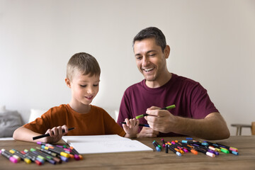 Cheerful Hispanic dad and cute son kid drawing in colorful pencils, markers, felt pens in paper...