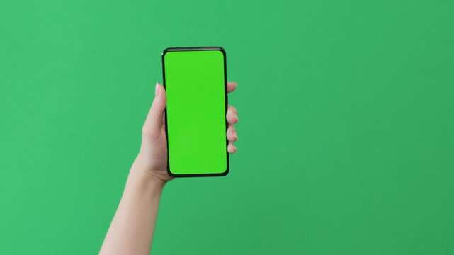 Young woman hand show smartphone with green screen on green background