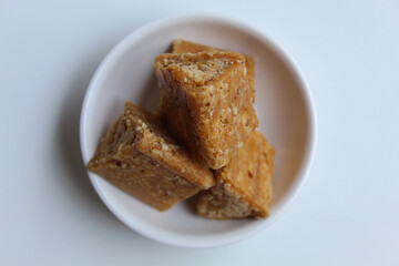 Enting-enting in triangle shape. Enting-enting is crushed peanuts mixed with sugar, Indonesia traditional snack. On small white bowl, isolated on white background