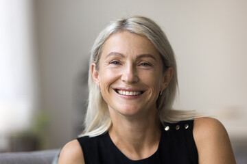 Head shot portrait 60 years old smiling grey haired lady on retirement looking at camera making video call enjoying happy life. Profile picture of beautiful stylish middle aged woman in social network