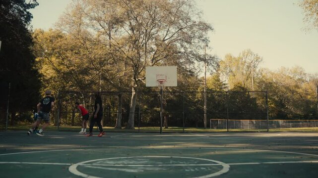 Young men playing basketball on an outdoor court on a sunny day