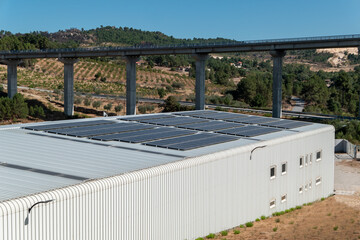 Edifício industrial com painéis solares no telhado, símbolo de sustentabilidade e tecnologia em harmonia com a ponte elevada ao fundo e a paisagem rural em Portugal