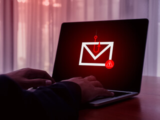 E-mail spam phishing scammer concept. Red warning symbol on envelope in fishing hook icon as bait on laptop screen, criminal hacker cyberattack sending scam malware spreading virus sms text message.