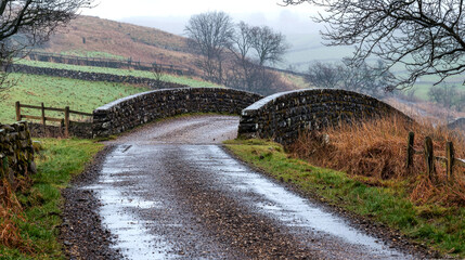 Stone bridge over a country road with rolling hills in the background.