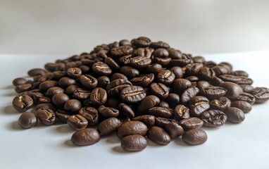 Fototapeta premium Coffee Beans: A small pile of roasted coffee beans, capturing their rich texture and color on a white background 