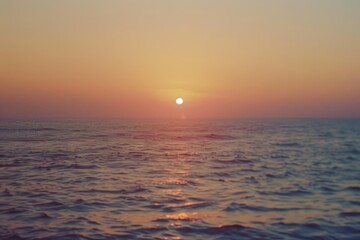 Obraz premium A serene sunset scene with the sun dipping below the horizon, reflecting off the calm ocean waters