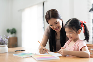 Asian mother helping her daughter with homework, sitting in living room interior, copy space.