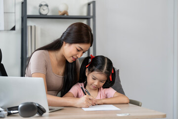 Working mother using laptop and help her daughter doing homework at home