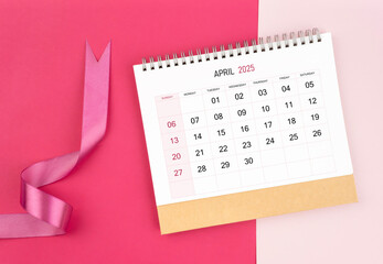 April 2025 desk calendar and pink ribbon on pink background.
