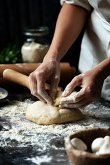 Hands kneading dough on a floured surface, with a rolling pin and baking ingredients in the background.