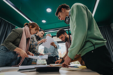 A group of college students collaborate on a project in a modern classroom while an elderly professor provides guidance and help, fostering teamwork and knowledge sharing.