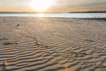 Sunset over a sandy beach with gentle ripples on the sand and a calm sea in the background. Peaceful scene ideal for themes of relaxation and nature.