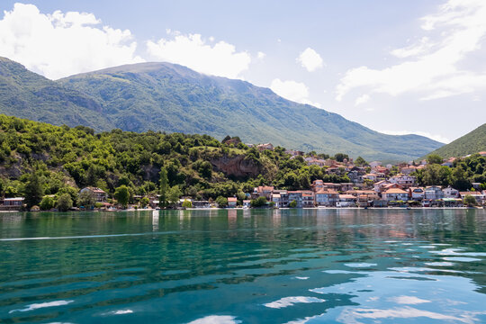 Lakeside town Trpejca nestled amidst lush green mountains of National Park Galicica, North Macedonia. Serene scene along shoreline of Lake Ohrid. Boat trip summer vacation. Balkan travel destination
