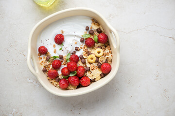 Yogurt bowl with fresh strawberry, granola and flakes, top view on a light-beige stone background, horizontal shot with space