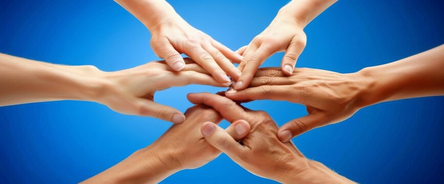 Close-up of hands put together in a gesture of team support and unity on a blue background. Conceptual image representing community, collaboration, teamwork, partnership.