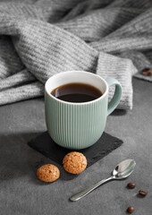 Espresso coffee in a mug on a dark background with cookies, spoon, coffee beans and a cozy gray sweater.