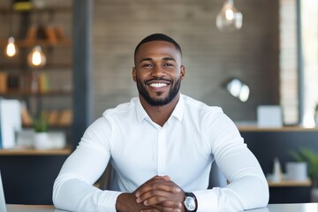 Obraz premium A well-dressed man in a white shirt beams with confidence as he sits at a table with his hands clasped, exuding a sense of success and approachability.