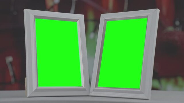 Two white picture frames with green chroma key screens placed side by side against blurred background perfect for photo or artwork mockups.