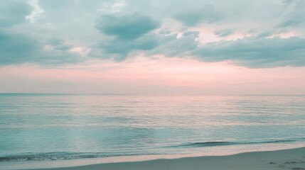 Fototapeta premium A calm beach scene at dawn, with muted pastel colors of light blue, gray, and soft pink reflecting in the water under a cloudy sky