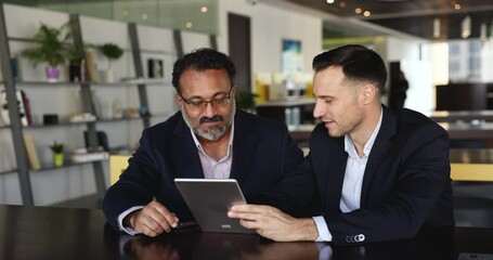 Two professionals, businessmen sitting at desk using tablet, discussing data, review and analyzing new application or information, working together on strategy, make decisions for their joint project