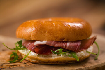 bagel sandwich with prosciutto and cream cheese on wood board