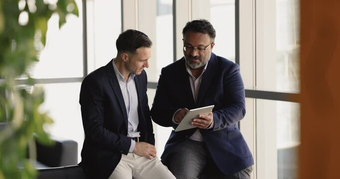 Two businessmen leading discussion, review new business proposal using digital tablet, shake hands, closing deal, reaching agreement, gesture of successful culmination of their strategic negotiations