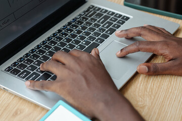 Close-up of hands typing on laptop keyboard situated on wooden desk, with partial view of screen...