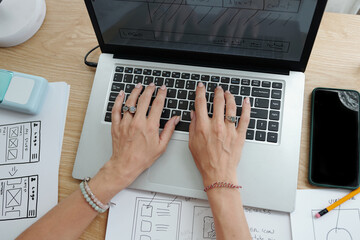 Hands working on laptop surrounded by sketches and notes, illustrating process of UI design and...