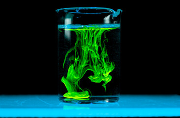 Dissolution and spread of a green substance in a flask with a clear liquid.