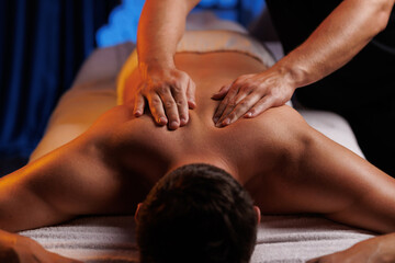 Physiotherapist massaging male patient with damaged shoulder muscle, treating sports injuries. Relaxing professional shoulder massage in cozy atmosphere, reboot on the weekend, end of difficult week.