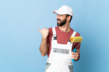 Adult painter man over isolated blue background pointing to the side to present a product