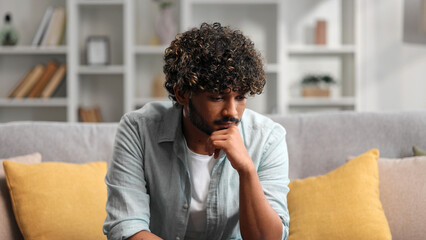 Bored millennial generation man sitting on sofa, feeling lonely at home. Unhappy young male...