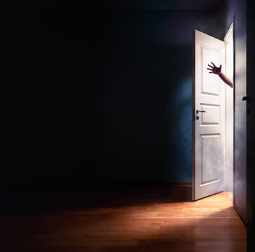 Horror door and hand. Scary halloween fantasy of a ghost or zombie or  in open closet. Spooky dark room in house. Creepy demon silhouette man in thriller movie or nightmare. Fog smoke and light.