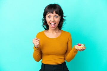 Young mixed race woman holding a tartlet isolated on blue background celebrating a victory in winner position