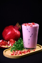 Pomegranate milk drink.  Detox. Proper nutrition. Pink drink in a glass with pomegranate seeds. Pomegranate seeds and greens on a stand.